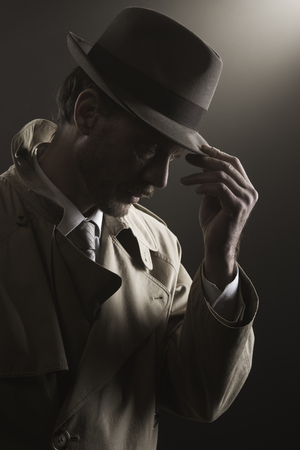 44583444 - detective adjusting his hat standing in the dark, film noir
